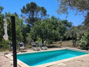 a swimming pool with two chairs and an umbrella at Le Mas Mélusine Chambres d hôtes avec piscine en oliveraie à Fayence in Fayence