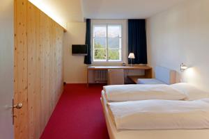 una camera d'albergo con due letti, una scrivania e una finestra di Hotel Castell a Zuoz