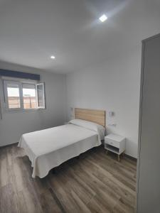 a white bedroom with a large bed and a window at Apartamentos Bolonia - M a n u e l a in Bolonia