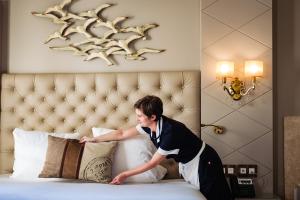a man putting pillows on a bed in a hotel room at Grand Hotel Des Sablettes Plage, Curio Collection By Hilton in La Seyne-sur-Mer