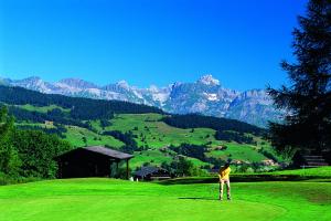 un hombre parado en un campo de golf con montañas en el fondo en Hotel Sylvana en Megève