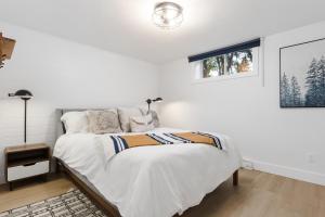 a white bedroom with a bed and a window at The Cozy Woodpecker Cottage in Notre-Dame-de-l'Île-Perrot