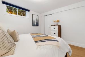 a white bedroom with a bed and a dresser at The Cozy Woodpecker Cottage in Notre-Dame-de-l'Île-Perrot