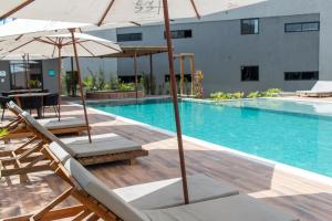 une piscine avec chaises et parasols à côté d'un bâtiment dans l'établissement Flat Villas Manatee Rota Ecológica dos Milagres, à Porto de Pedras