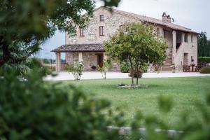 阿西西Agriturismo - La Campagna di San Francesco的一座大石头建筑,院子内有一棵树