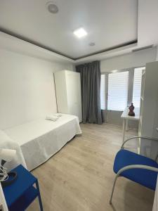 a bedroom with a white bed and a blue chair at AT Paseo Ficus Centenario in Almería
