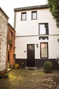 a white house with a black door on a brick street at La Petite Maison in Tournai