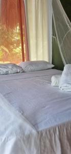 a bed with white sheets and pillows next to a window at Zirumake Tayrona Dentro del Parque Tayrona in El Zaino