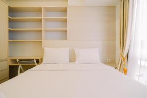 a bedroom with a bed with white pillows and shelves at Warm and Well Designed 2BR Tokyo Riverside PIK 2 Apartment By Travelio in Rawalembang