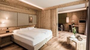 a bedroom with a large white bed in a room with wooden walls at Hotel Weiher Green Lake in Falzes