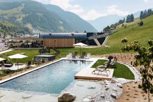 a swimming pool with chairs and a building and mountains at Hotel Roslehen in Grossarl