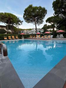 a large blue swimming pool with chairs and umbrellas at Casa Bianca Village Apartments in Lignano Sabbiadoro