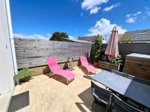a patio with pink chairs and a table and an umbrella at FLEUR DE SEL logement de 21m2 avec prêt vélos, cuisine et sdb privées avec terrasse clôturée de 17m2 in Batz-sur-Mer