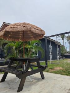a picnic table with a straw umbrella and palm trees at Penarik baru homestay in Penarek
