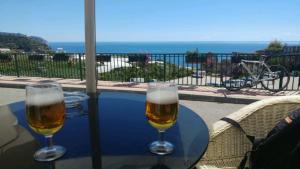 two glasses of beer sitting on a table near a pool at Apartamentos Balcón de Maro in Maro