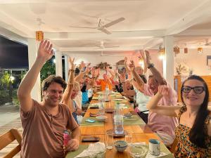 Eine Gruppe von Menschen, die an einem Tisch sitzen und die Hände in der Luft haben in der Unterkunft Ocean Voice Beach Resort & Diving in Nolhivaranfaru