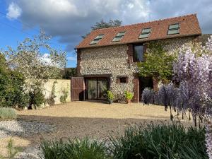una vecchia casa in pietra con fiori viola di fronte di La petite Maison en Normandie a Muids