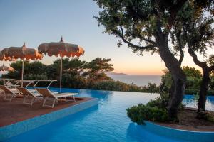 a pool with chairs and umbrellas and the ocean at Boutique Hotel Torre Di Cala Piccola in Porto Santo Stefano