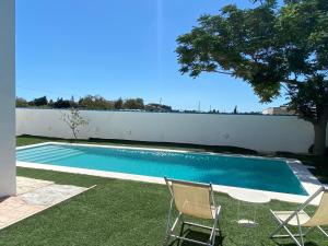 a swimming pool with two chairs and a tree at Alojamiento Rural Al´Mare in Conil de la Frontera