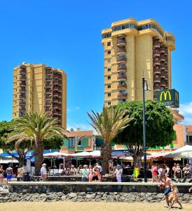 Un grupo de personas caminando por la playa cerca de edificios. en Apartamento Torres del Sol en Playa Las Vistas - Los Cristianos, en Arona