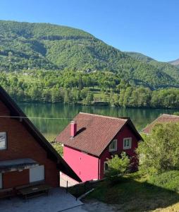 a red house next to a lake with a mountain at Apartman Plivsko Jezero Jajce in Jajce