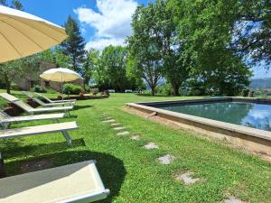 a group of lawn chairs with an umbrella and a pool at Casa Vacanze Le Corone in Otricoli