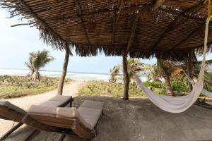 a hammock and chair under a straw umbrella on a beach at Cabanas Adobe Frente Al Mar in Puerto Escondido