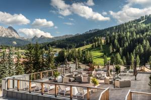 Un balcón con sillas, mesas y una montaña. en Hotel Diamant en San Cassiano