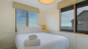 a white bedroom with a white bed with windows at Shamrock 1 in Mount Hotham