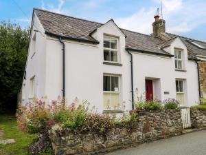 a white house with a stone wall and flowers at Panteg Cottage, Newport in Newport Pembrokeshire