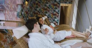 two people laying on a bed in front of a mirror at MANNI das Hotel in Mayrhofen