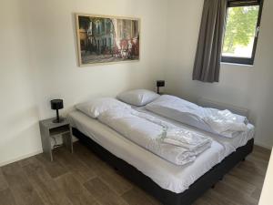 a bed with white sheets and a picture on the wall at Enkhuizer Strand Chalet AusZeit Haus Nr 243 in Enkhuizen