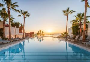 a pool with palm trees and the ocean at sunset at Spirit Hotel Benalmadena Beach in Benalmádena