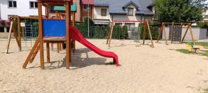 a playground with a red slide in the sand at Underground Apartament in Łomża