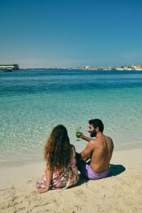 a man and woman sitting on the beach drinking beer at Triumph White Sands Hotel in Marsa Matruh
