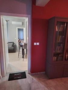 a living room with a red wall and a room with a tv at Χαίρε, ξεΐνε, παρ' αμμι φιλησεαι in Tríkala