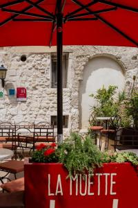 a restaurant with a red umbrella and tables and chairs at Hôtel La Muette in Arles