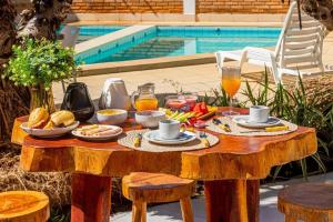 a wooden table with breakfast foods on it next to a pool at Pousada Corais Barra in Barra de São Miguel +55 photos
