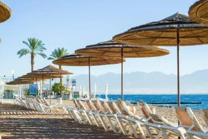 una fila de sillas y sombrillas en una playa en דירה עם מרפסת במתחם סי סייד - By Edomlux, en Eilat