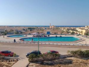 a swimming pool with two cars parked in a parking lot at شاليه بقرية القصر السياحية للايجار ب مطروح إمتداد شاطيء الأبيض حمام السباحة في القرية به صيانه in Marsa Matruh