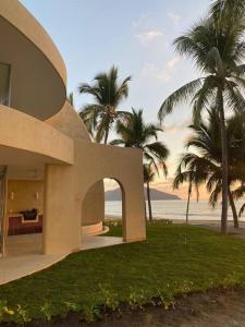 a building with palm trees in front of the ocean at Hermosa villa a pie de playa in Barra de Potosi