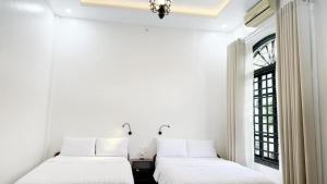 two beds in a white room with a window at Rose's Homestay Hue in Hue