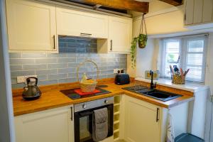 eine Küche mit weißen Schränken und einer Holzarbeitsplatte in der Unterkunft The Hangmans Cottage in Abbotskerswell