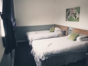 two beds in a room with white sheets and green pillows at Brewers Lodge in Blackwood