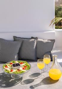 a table with a salad and two glasses of orange juice at Quartano Suites by Heliessa, Adults Only in Naousa
