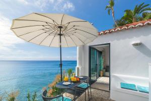 a table with an umbrella next to the ocean at OurMadeira - Cottage do Mar, secluded in Arco da Calheta