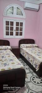 two beds in a room with pink walls and a window at Villa El kheer in `Ezbet el-Dabdûba +1 photo
