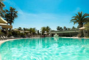 a large swimming pool with palm trees and a building at UNAHOTELS MH Matera in Matera