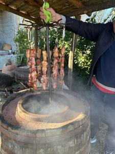 une personne fait cuire de la viande sur un gril extérieur dans l'établissement Guest house and cellar MAMULI, à Tʼerjola