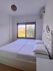 a white bedroom with a bed and a window at Viluni Coast Apartment in Velipojë